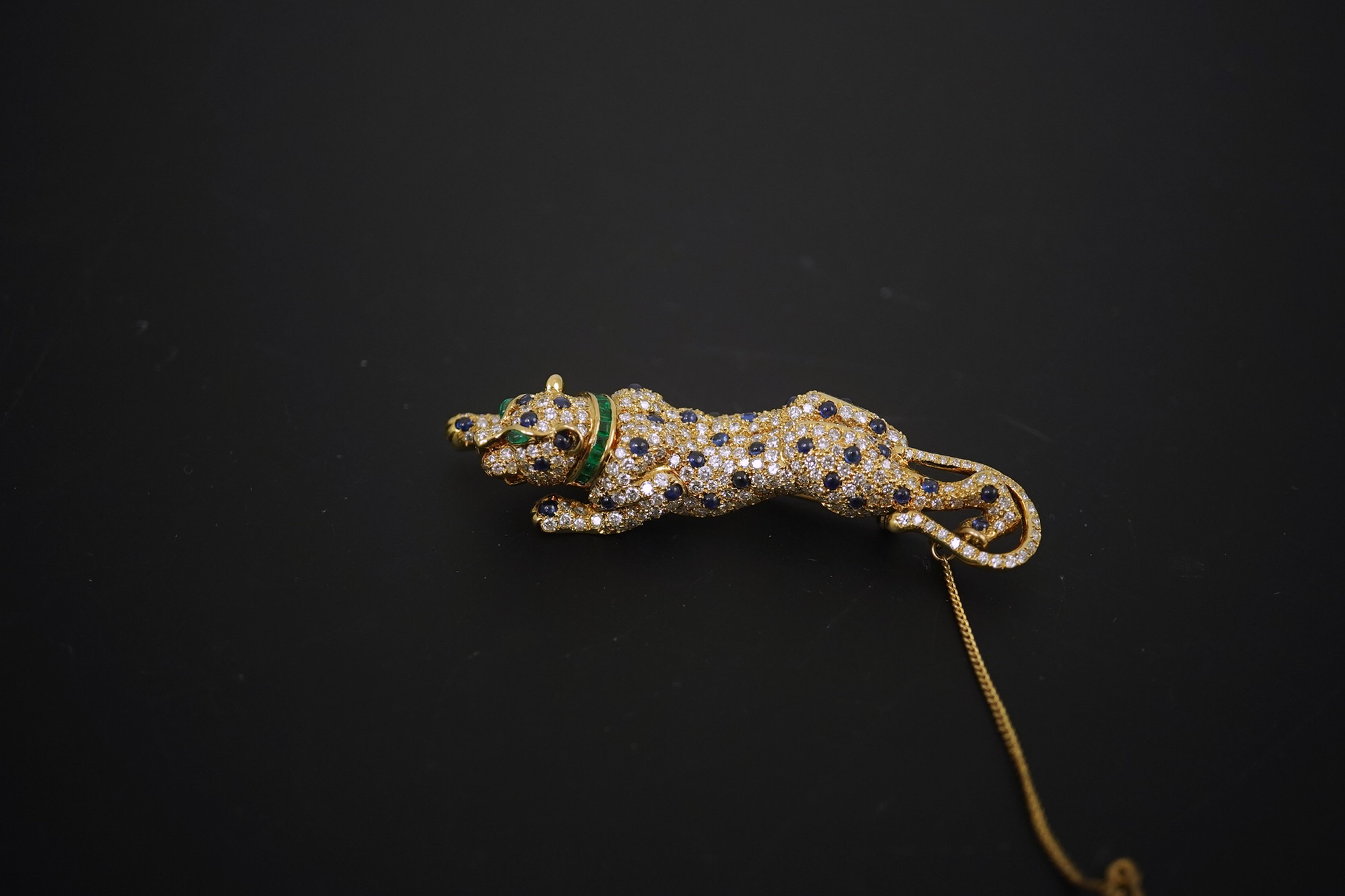 A modern Cartier style 18k gold, sapphire, emerald and diamond cluster set stalking panther brooch